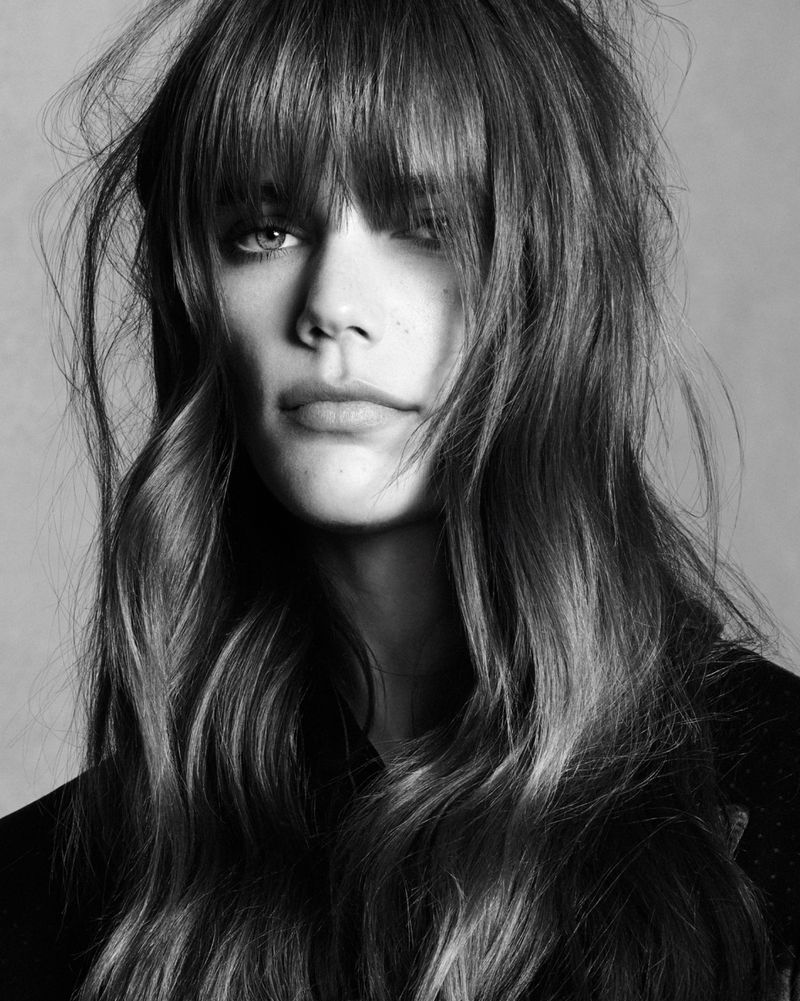 Close-up monochrome portrait of model Betsy Gaghan with long textured hair and bangs against a neutral background.