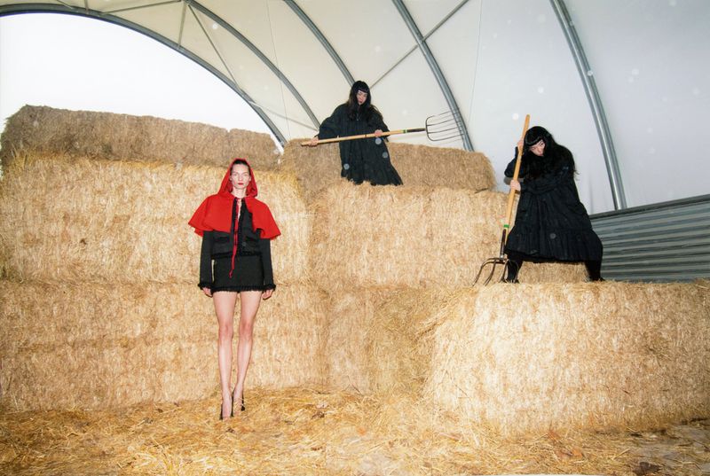 Three models posed among stacked hay bales inside an arched agricultural structure for Re-Edition Magazine