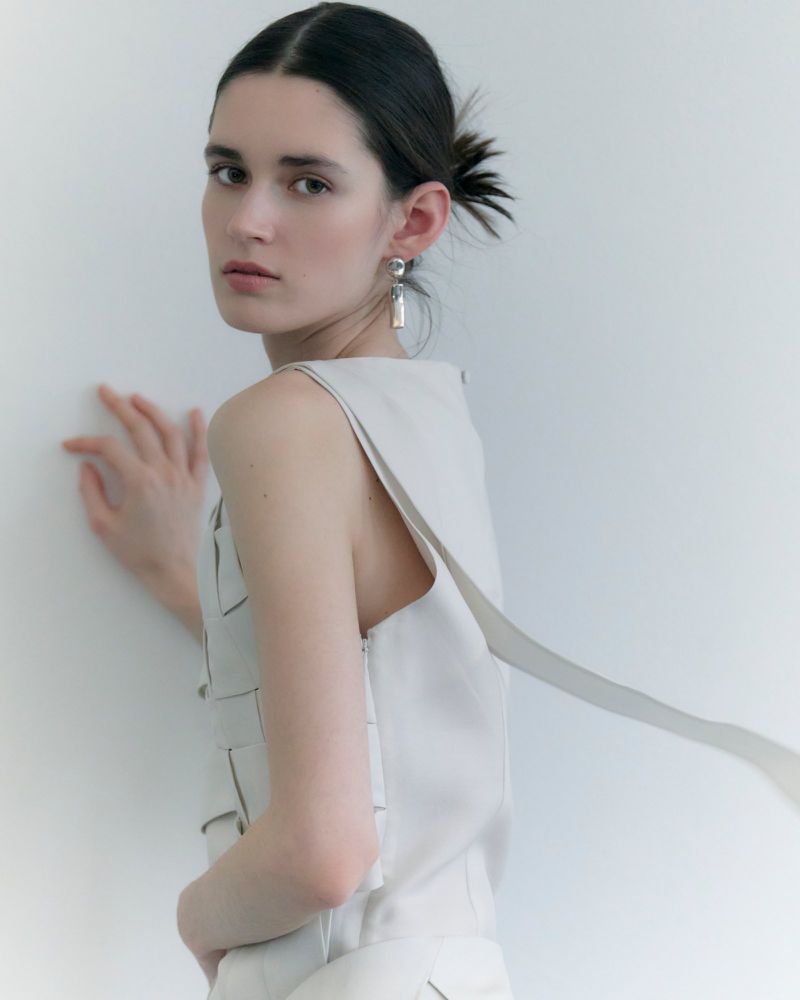Portrait of a woman wearing a light-coloured sleeveless top and dangling earrings against a white background.