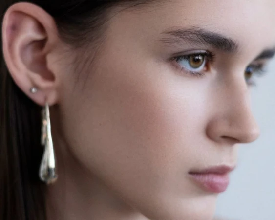 Close-up portrait of a woman wearing a silver drop earring against a neutral background