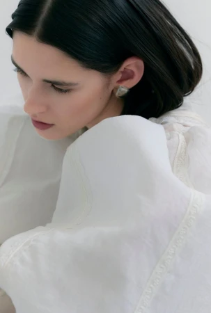 Close-up portrait of a woman with dark hair wearing a white textured blouse against a plain background