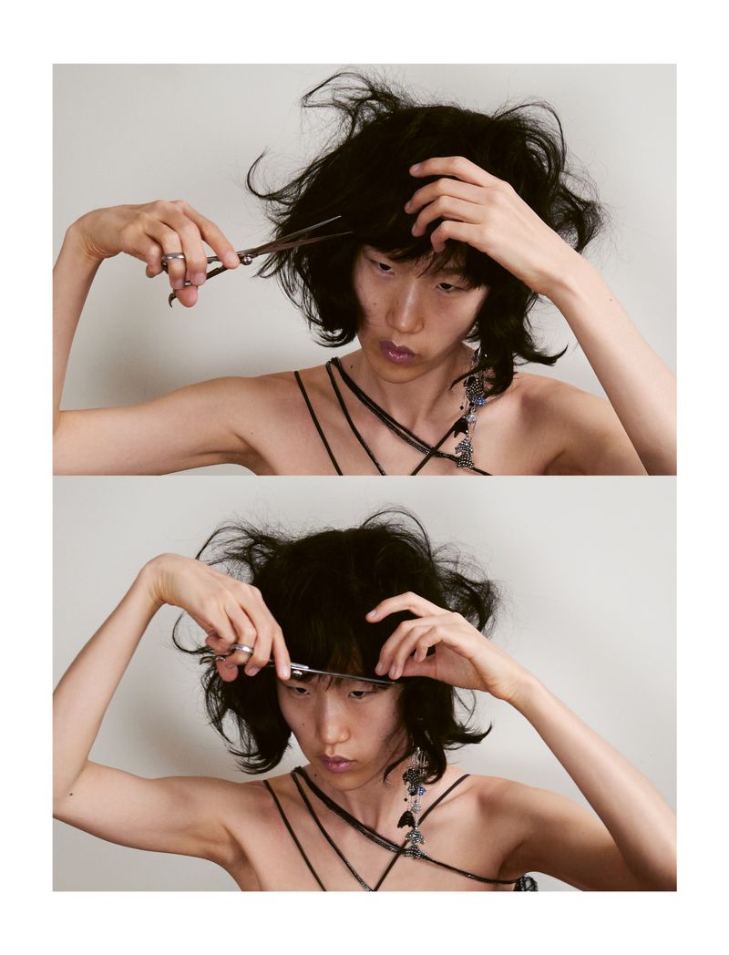 Model Jiashan Liu cutting her own black hair with scissors against a plain white background for Whatevr Magazine.