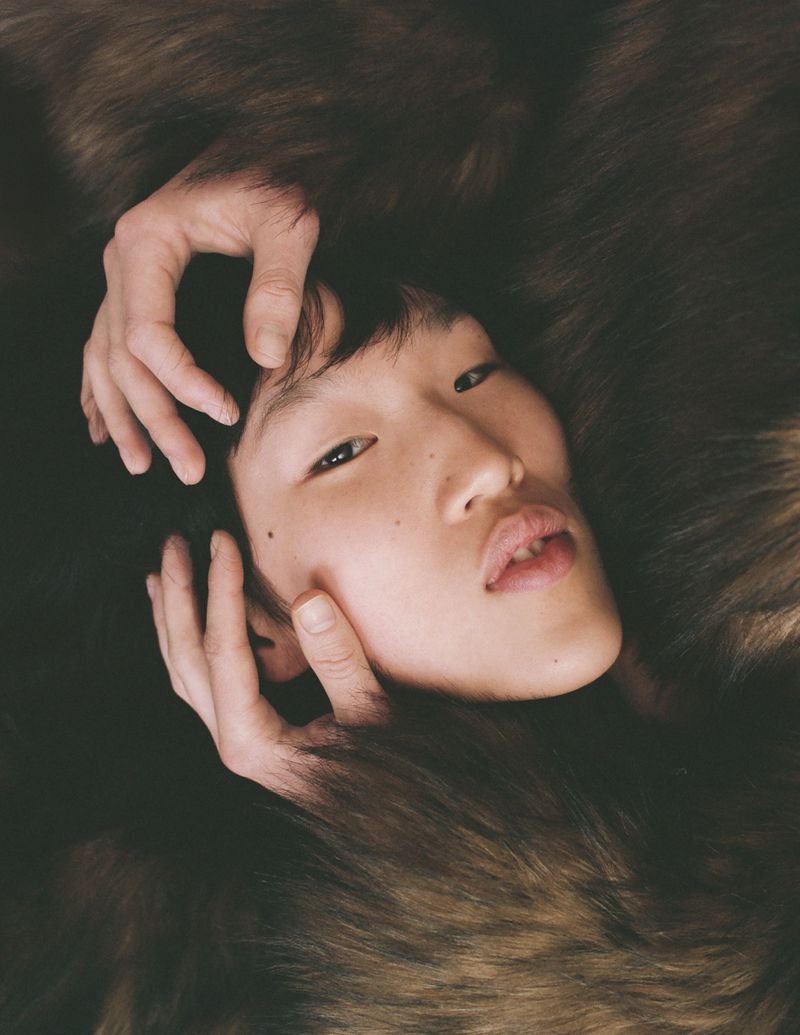 Close-up portrait of model Jiashan Liu with hands framing face against a dark textured background for Whatevr Magazine.