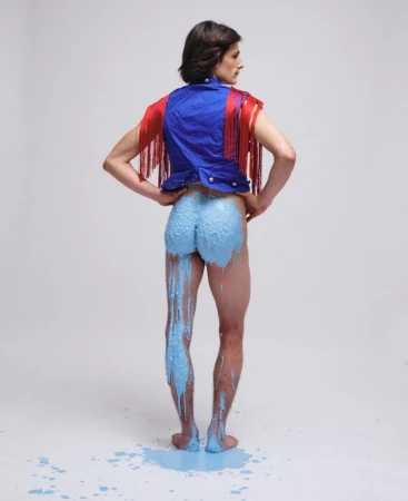 Model from behind wearing a blue vest with red fringe and blue paint dripping down his legs against a white background