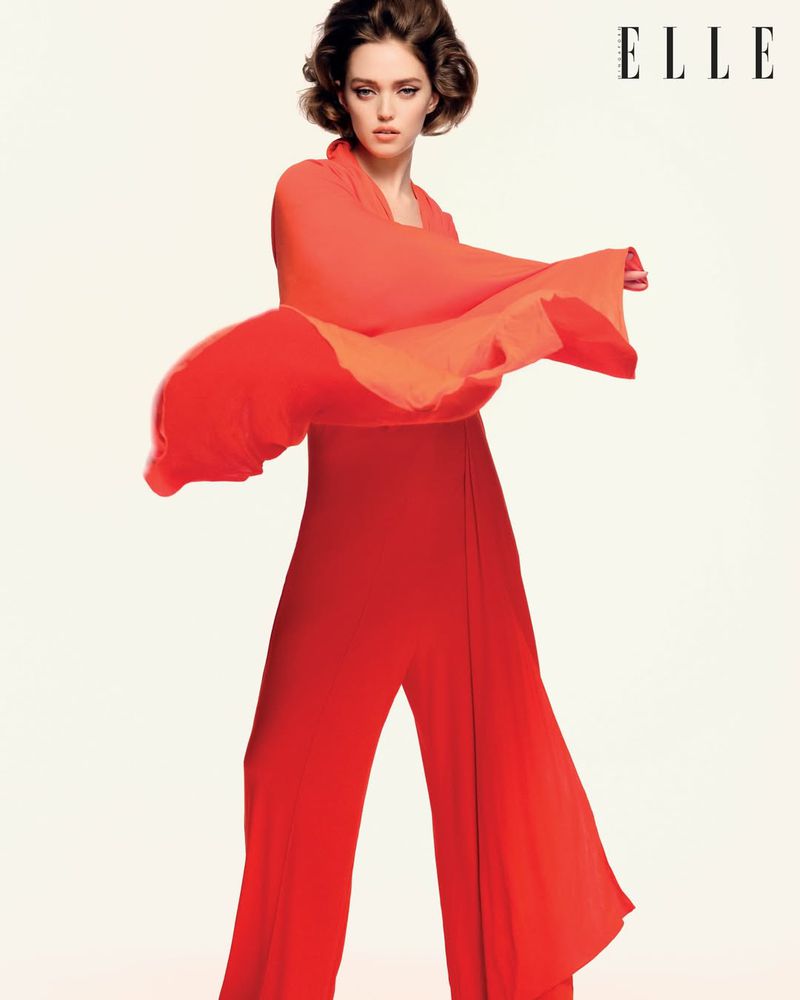 Model Polly Domashych wearing a vibrant red dress against a plain light background for Elle Singapore March 2026 editorial.