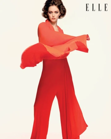 Model Polly Domashych wearing a vibrant red dress against a plain light background for Elle Singapore March 2026 editorial.