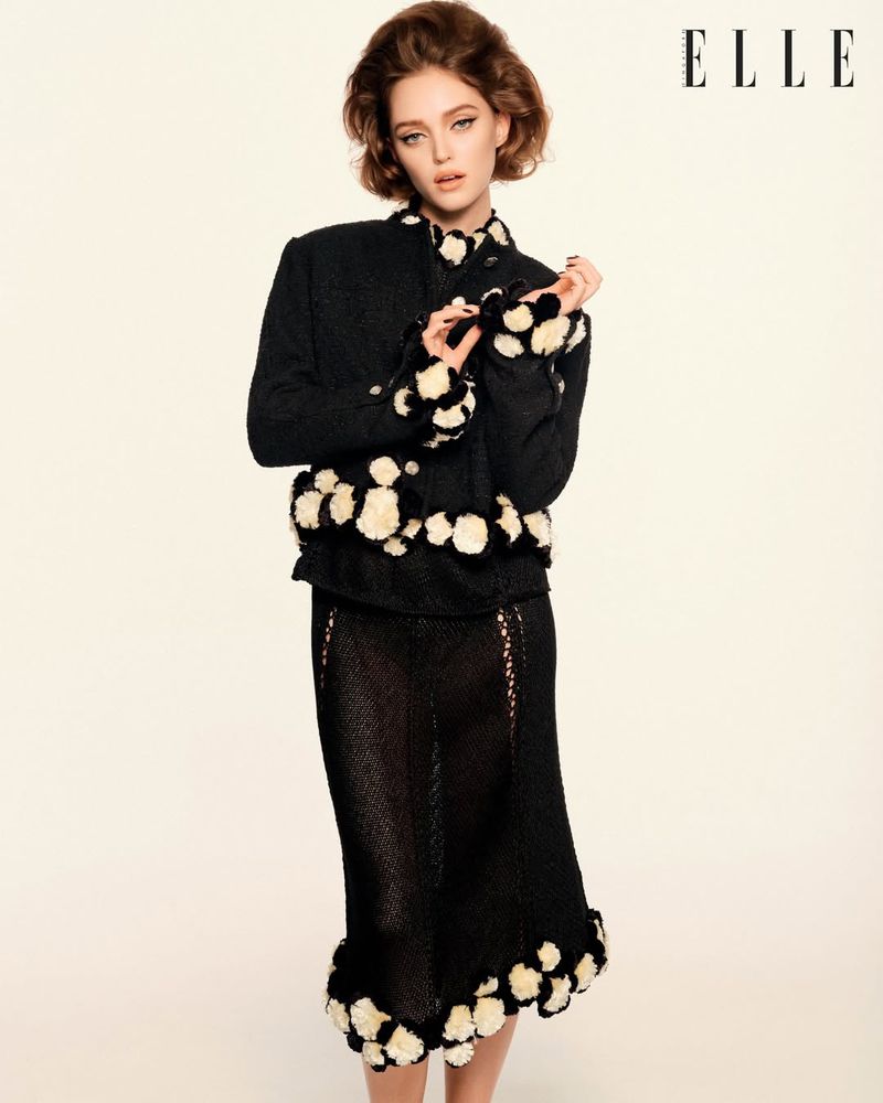 Model Polly Domashych wearing a black patterned jacket and matching skirt against a plain studio background for Elle Singapore.