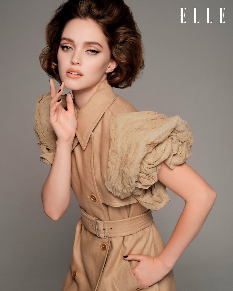 Model Polly Domashych in a tan belted dress with voluminous sleeves posing against a plain grey backdrop for Elle Singapore March 2026.