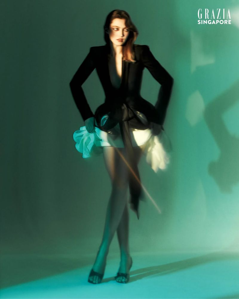 Model Polly Domashych in a structured black blazer with white underskirt against a green backdrop, photographed by Joel Low.