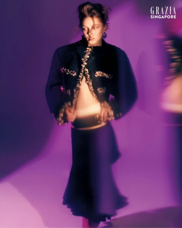 Model in dark textured jacket and skirt posing against a vibrant purple studio background with motion blur effect