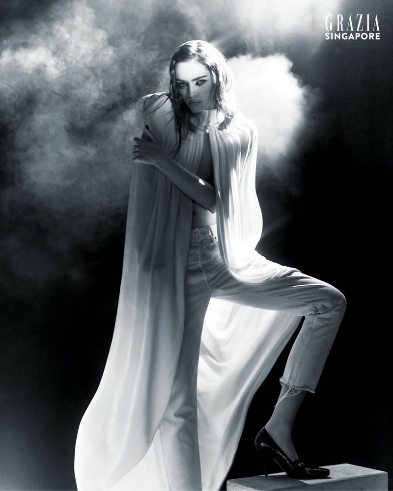 Model Polly Domashych wearing a flowing white cape and trousers amid theatrical smoke for Grazia Singapore by photographer Joel Low.