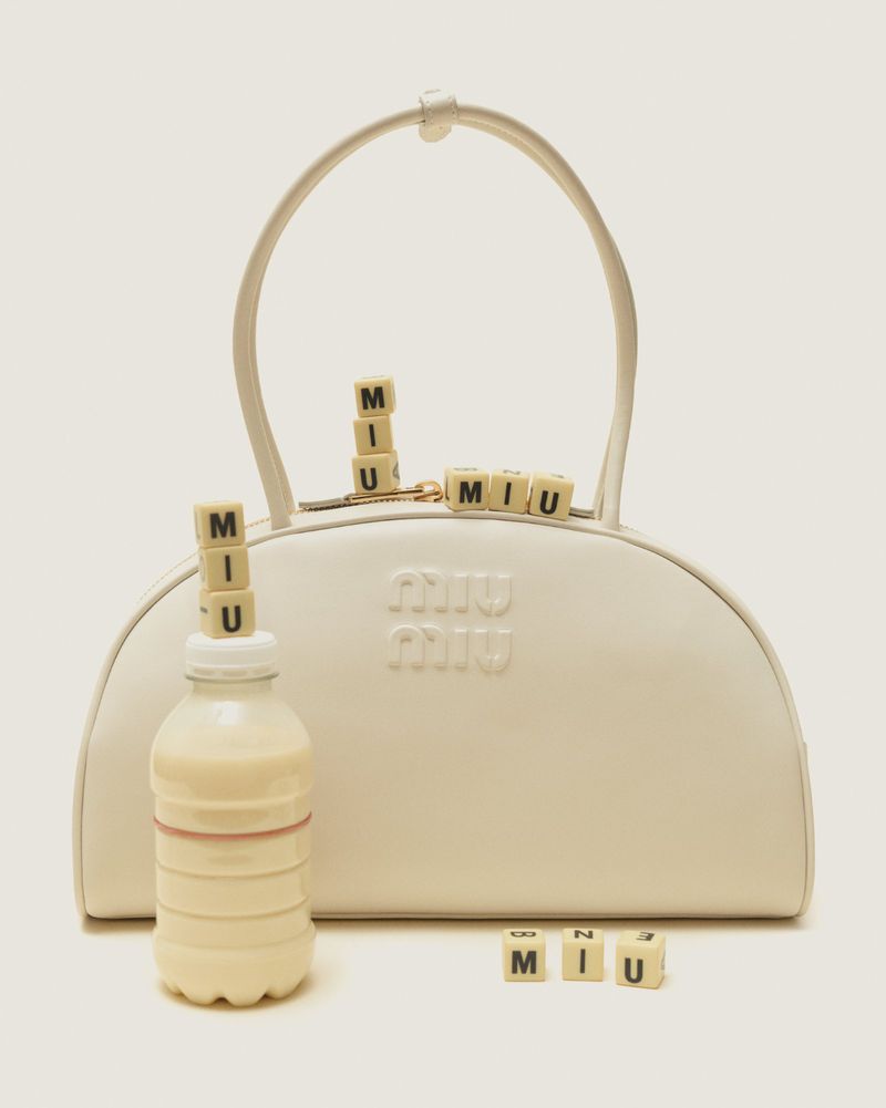 Elegant ivory Miu Miu handbag with letter tiles spelling 'MIU' and a matching cream bottle, showcasing luxury fashion photography.