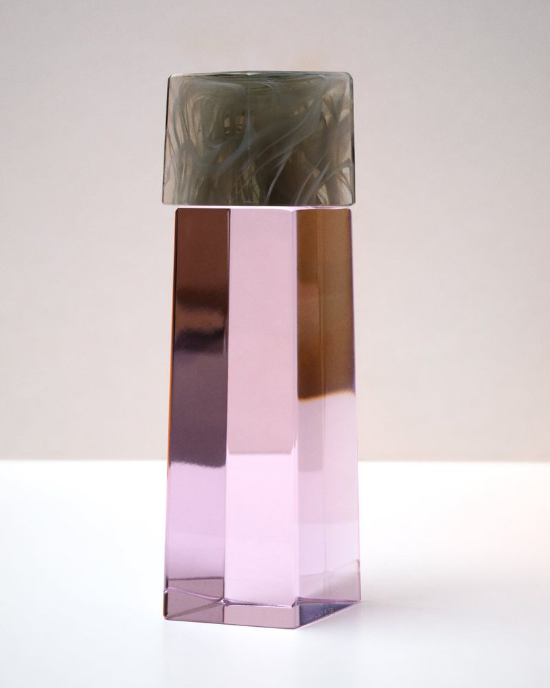 Cylindrical glass bottle with metallic pink faceted body and dark translucent cap on a white surface.