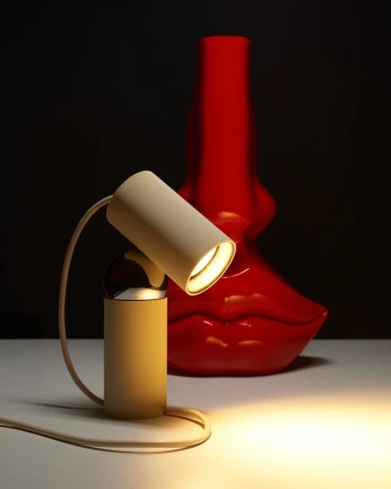 Modern beige desk lamp glowing beside a glossy red sculptural lip vase against a dark background