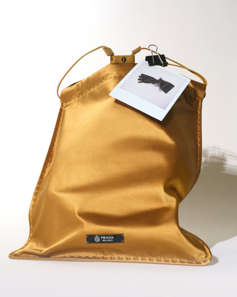 Gold satin Prada dust bag against a white seamless background with a pinned Polaroid photo