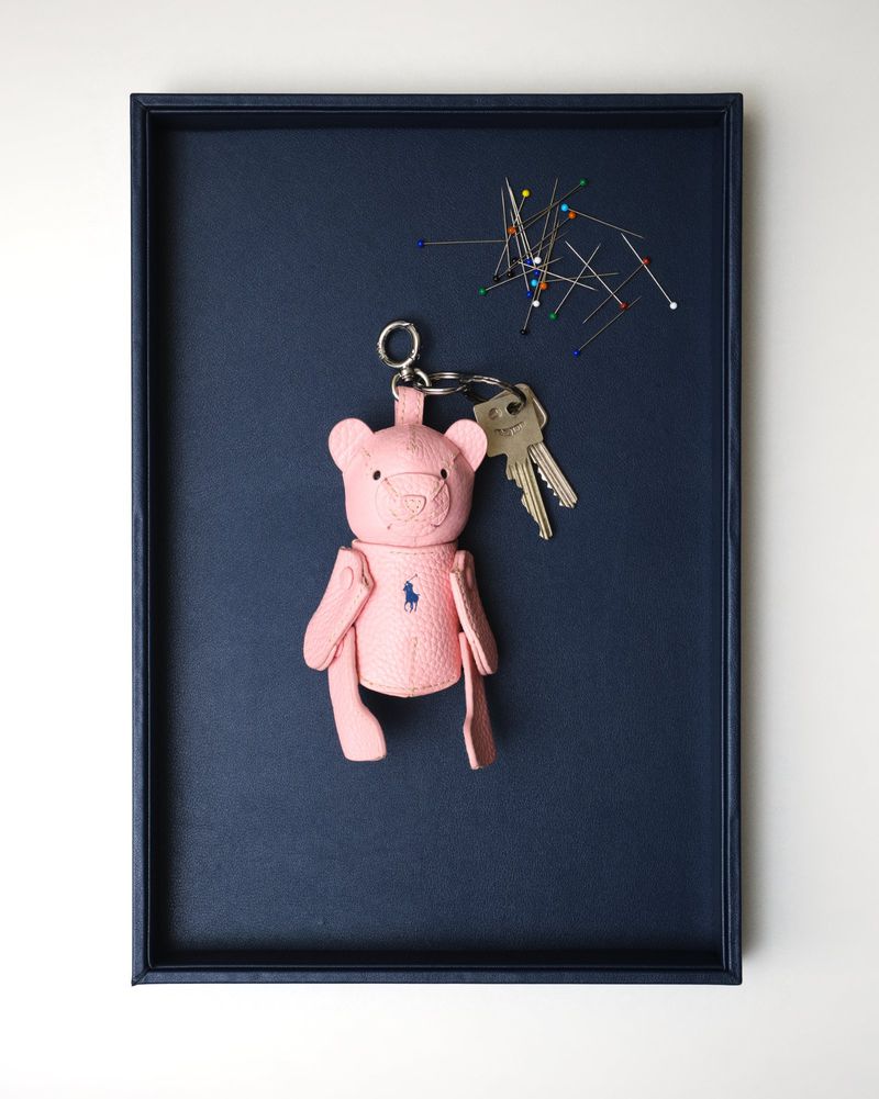 Pink leather bear keychain and metal keys with colorful sewing pins resting inside a dark blue tray