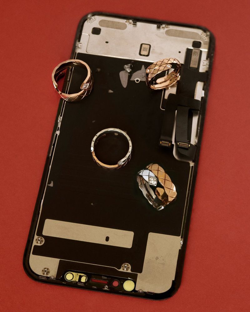 Disassembled smartphone resting on a solid red surface with four metallic quilted rings arranged on top