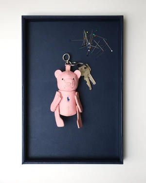 Pink leather bear keychain and metal keys with colorful sewing pins resting inside a dark blue tray