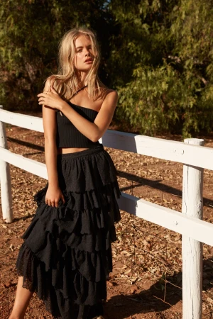 Blonde female model wearing a black crop top and tiered skirt posing by a white fence