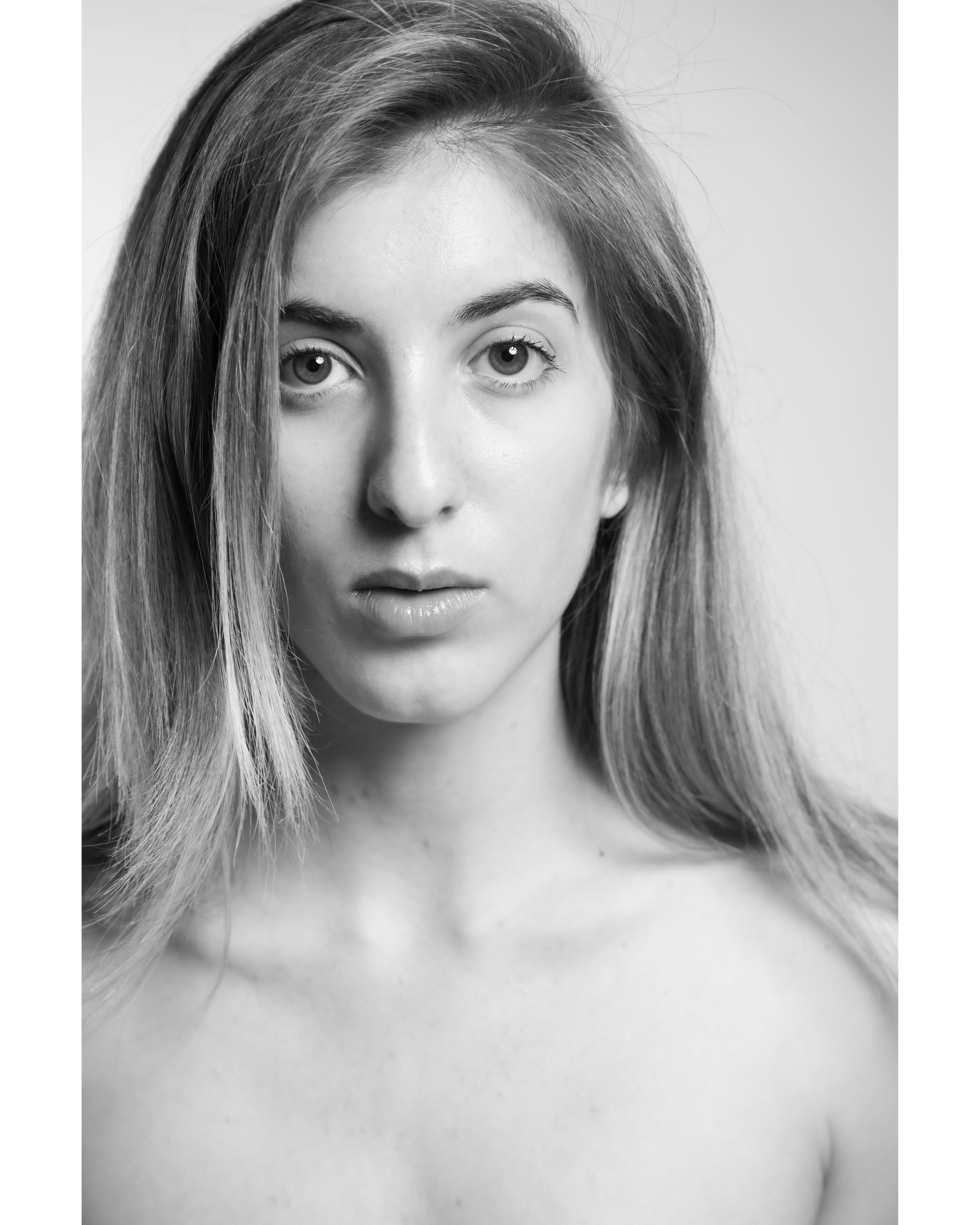 Monochrome portrait of a young adult woman with long hair, fair skin, and a neutral expression, against a plain light background.