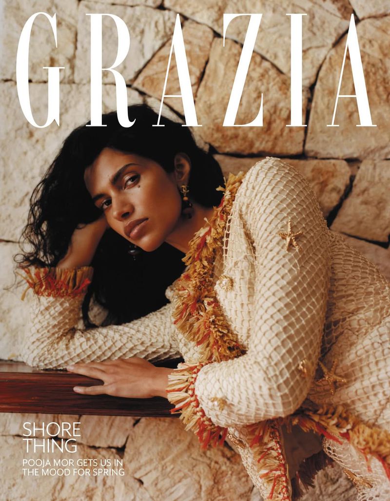 Model Pooja Mor leaning against a rustic stone wall wearing a textured cream dress for Grazia UK magazine.