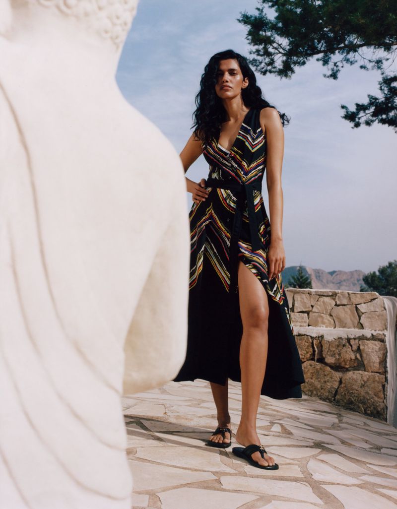 Model Pooja Mor in a patterned dress posing outdoors near a stone wall for Grazia UK