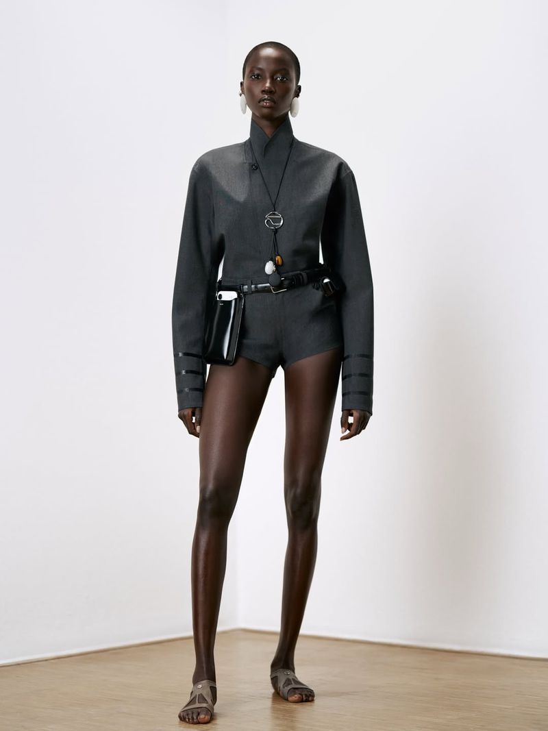 Model Anok Yai wearing a grey jacket and shorts with a black belt bag in a Coperni collection portrait