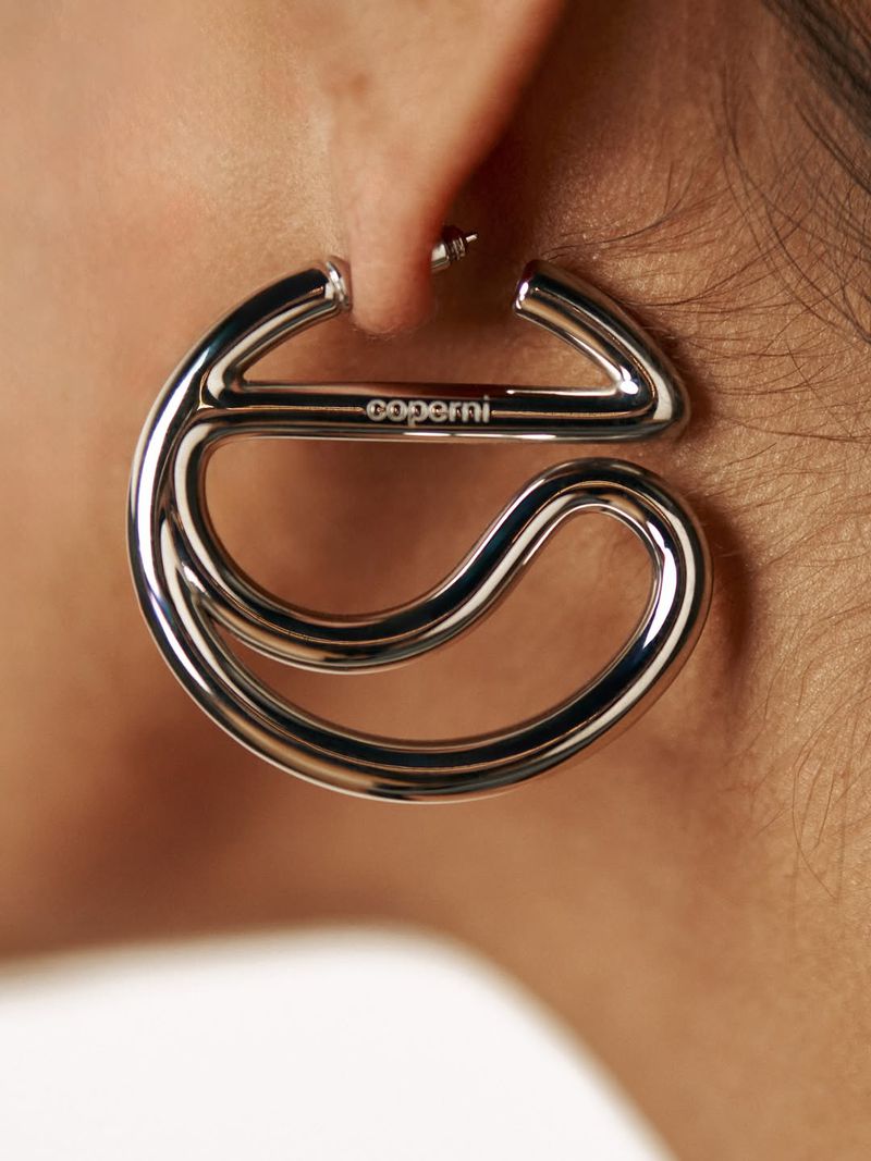 Close-up of a silver hoop earring featuring the Coperni logo worn on an earlobe