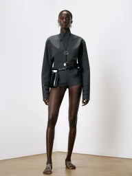 Model Anok Yai wearing a grey jacket and shorts with a black belt bag in a Coperni collection portrait