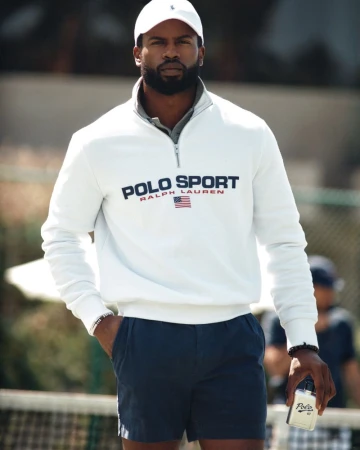 Black man wearing a white quarter-zip sweatshirt and holding a Ralph Lauren Polo Sport fragrance bottle outdoors.