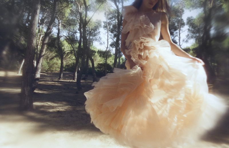 Model in a voluminous layered ruffle dress posing outdoors in a sunlit pine forest for Ulla Johnson Ulla eau de parfum.