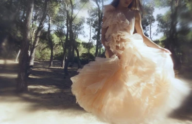 Model in a voluminous layered ruffle dress posing outdoors in a sunlit pine forest for Ulla Johnson Ulla eau de parfum.
