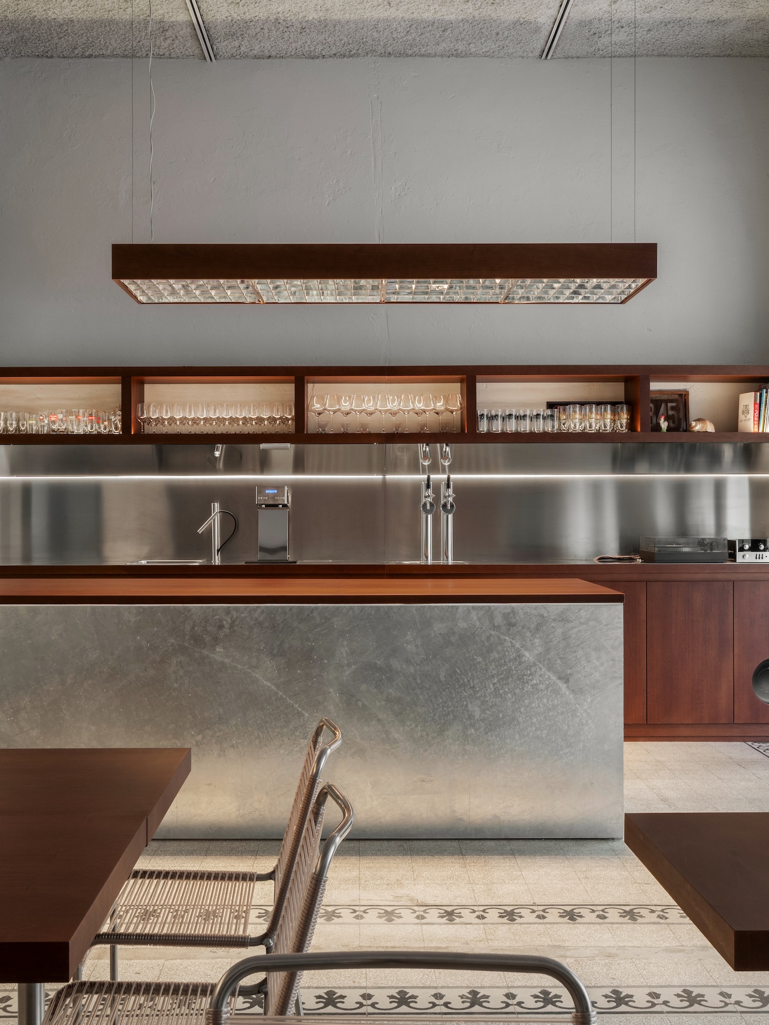 Modern interior architectural photograph of a sleek bar counter with metallic finish and warm wooden shelving