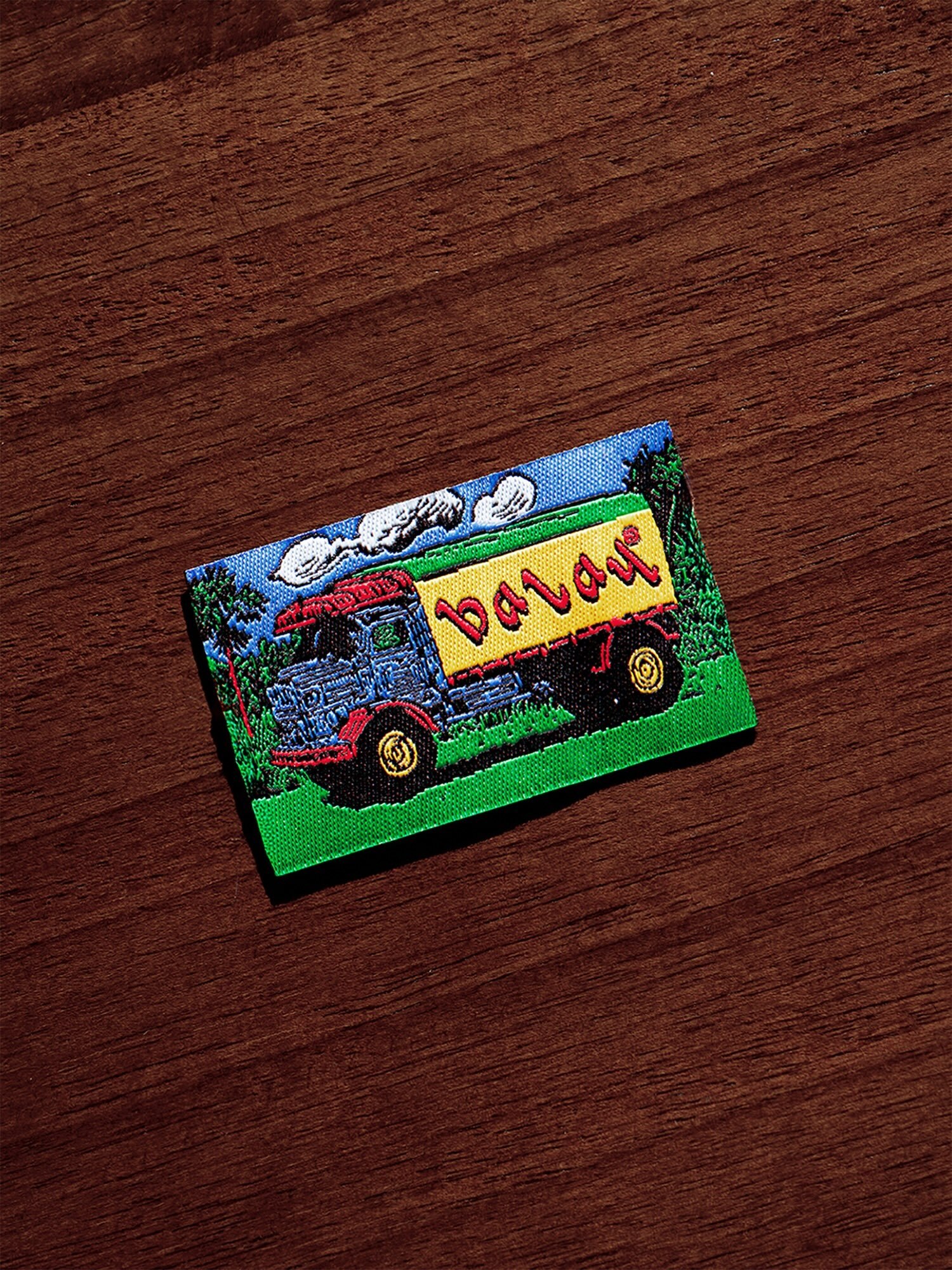 Embroidered patch showing a blue truck with yellow cargo on a green field resting on a dark wood grain surface