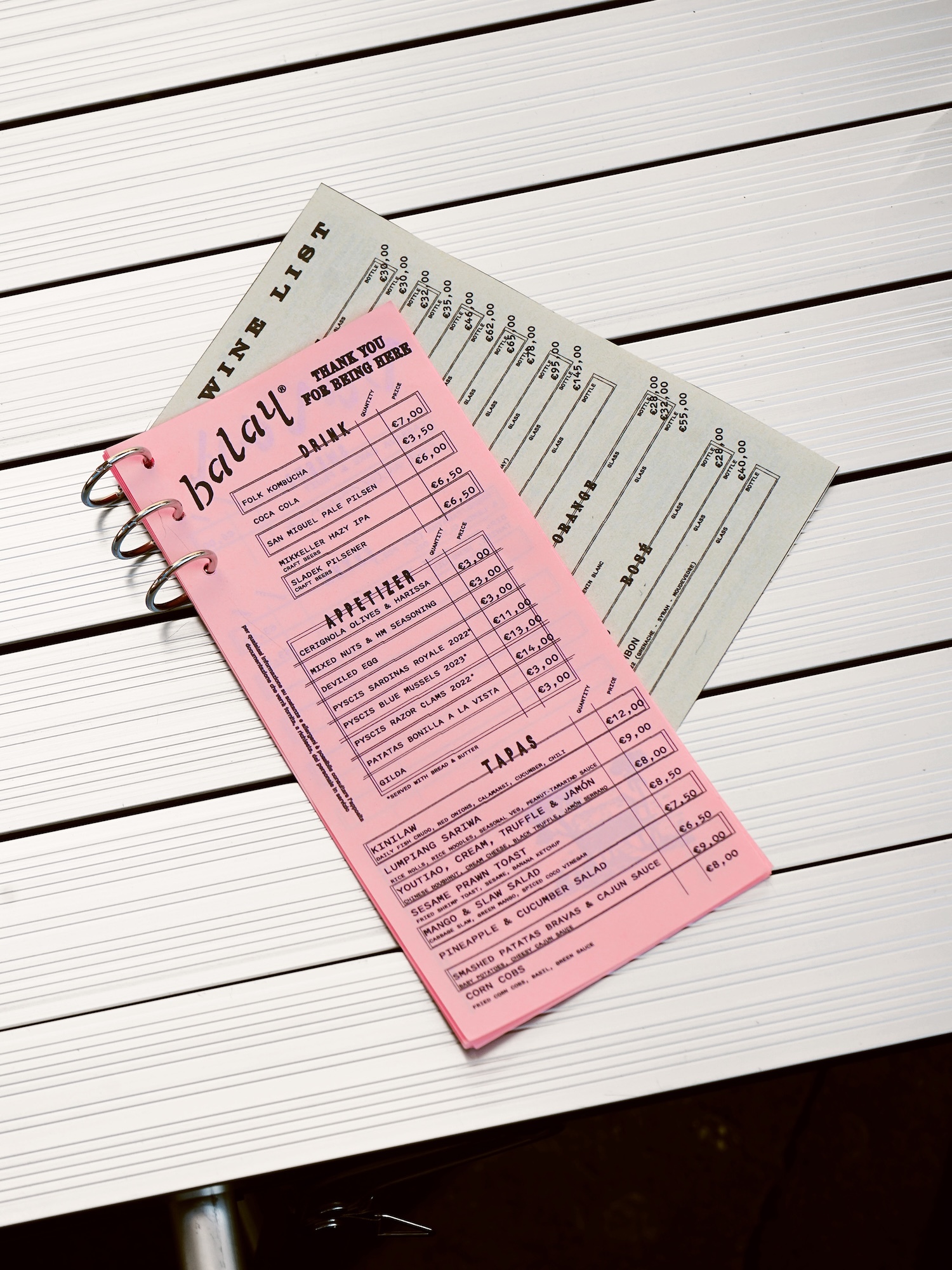 Pink Balay restaurant menu and grey wine list resting on a slatted white tabletop.