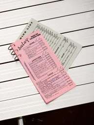 Pink Balay restaurant menu and grey wine list resting on a slatted white tabletop.