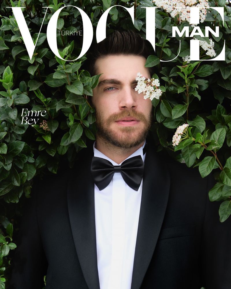 Vogue magazine cover featuring a handsome man in a tuxedo, framed by lush green foliage and delicate white flowers for a striking editorial shot.