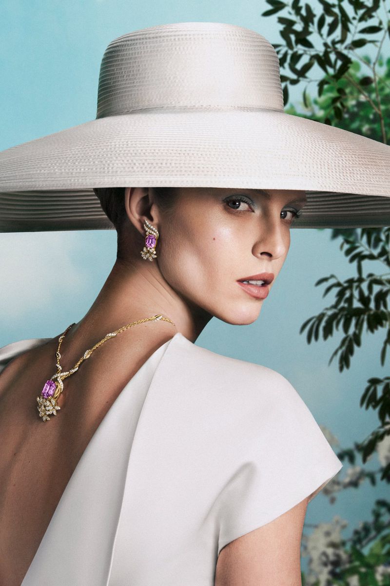 Model wearing a wide-brimmed white hat, diamond necklace, and earrings against an outdoor backdrop for Tiffany & Co.