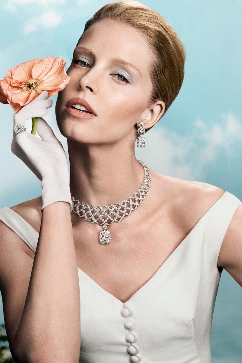 Model Abby Champion wearing high jewelry diamond necklace and earrings with a peach flower against a blue sky background for Tiffany & Co.