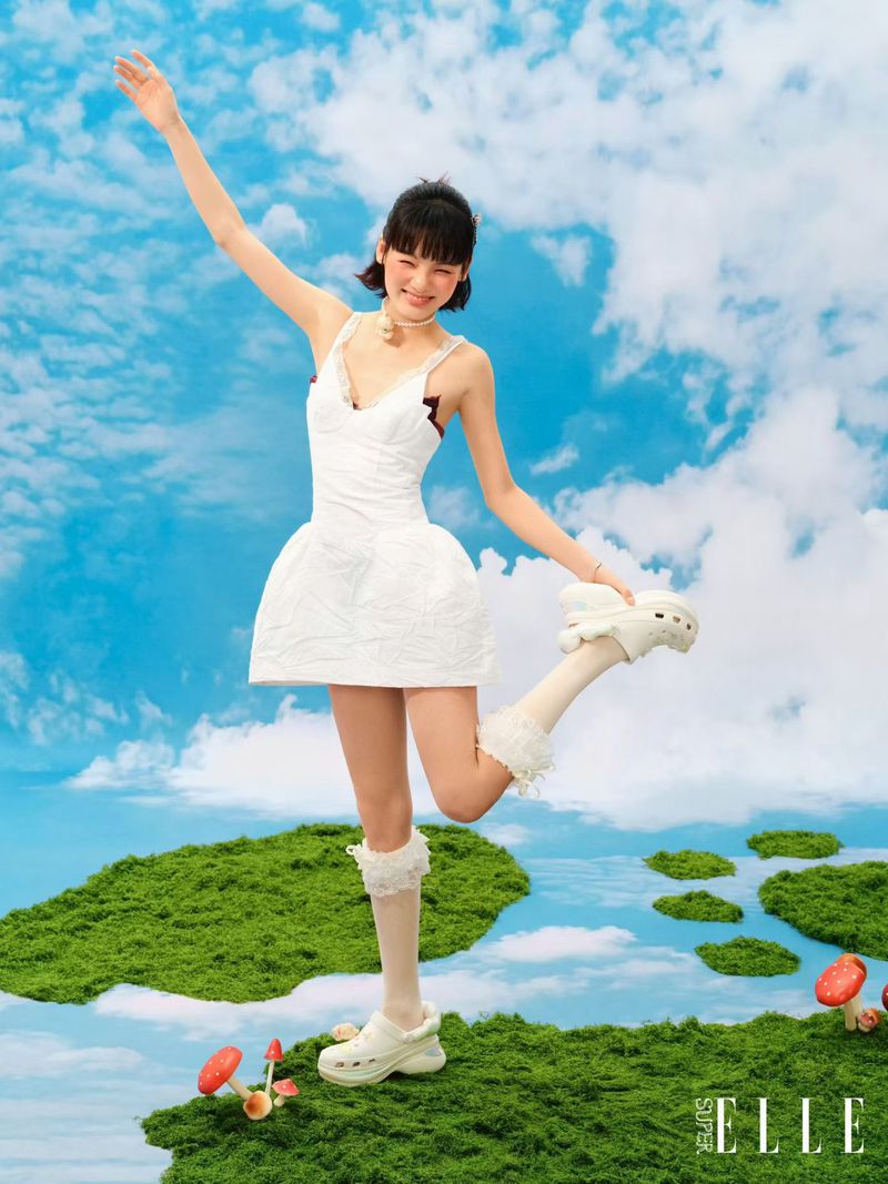 Young woman in a white dress holding up her shoe against a whimsical sky and mossy ground backdrop