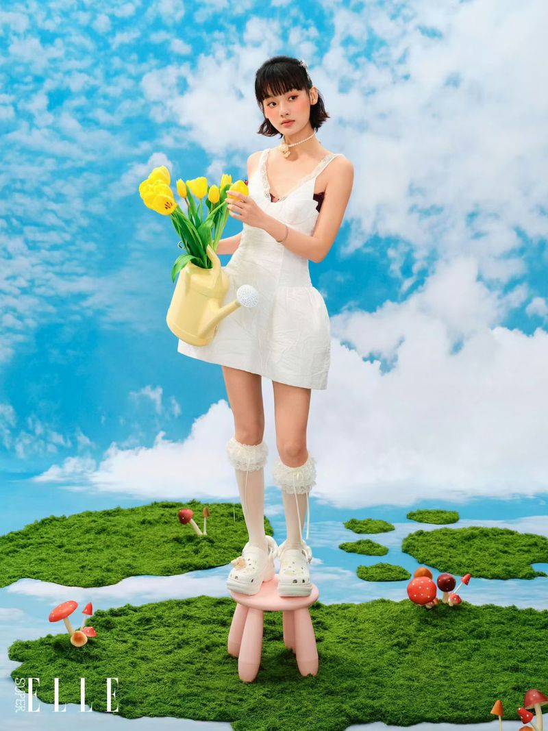 Model in white dress holding yellow tulips and watering can standing on a stool against a blue sky background for SuperELLE China