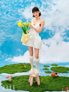 Model in white dress holding yellow tulips and watering can standing on a stool against a blue sky background for SuperELLE China
