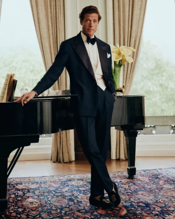 Man wearing a navy tuxedo leaning against a black piano in a classic room