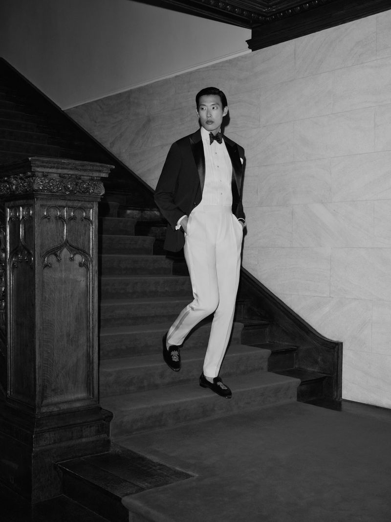 Man in a formal tuxedo descending a grand staircase in a black and white fashion portrait.