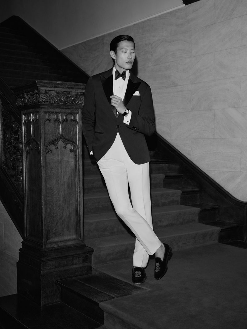 Man wearing a formal tuxedo with white trousers standing on a grand staircase for Polo Ralph Lauren formalwear.