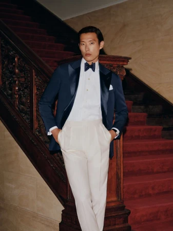 Man wearing a navy tuxedo jacket with white trousers standing on a grand staircase with red carpet