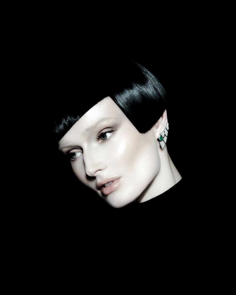 Close-up portrait of a woman with short dark hair and an ear cuff against a black background