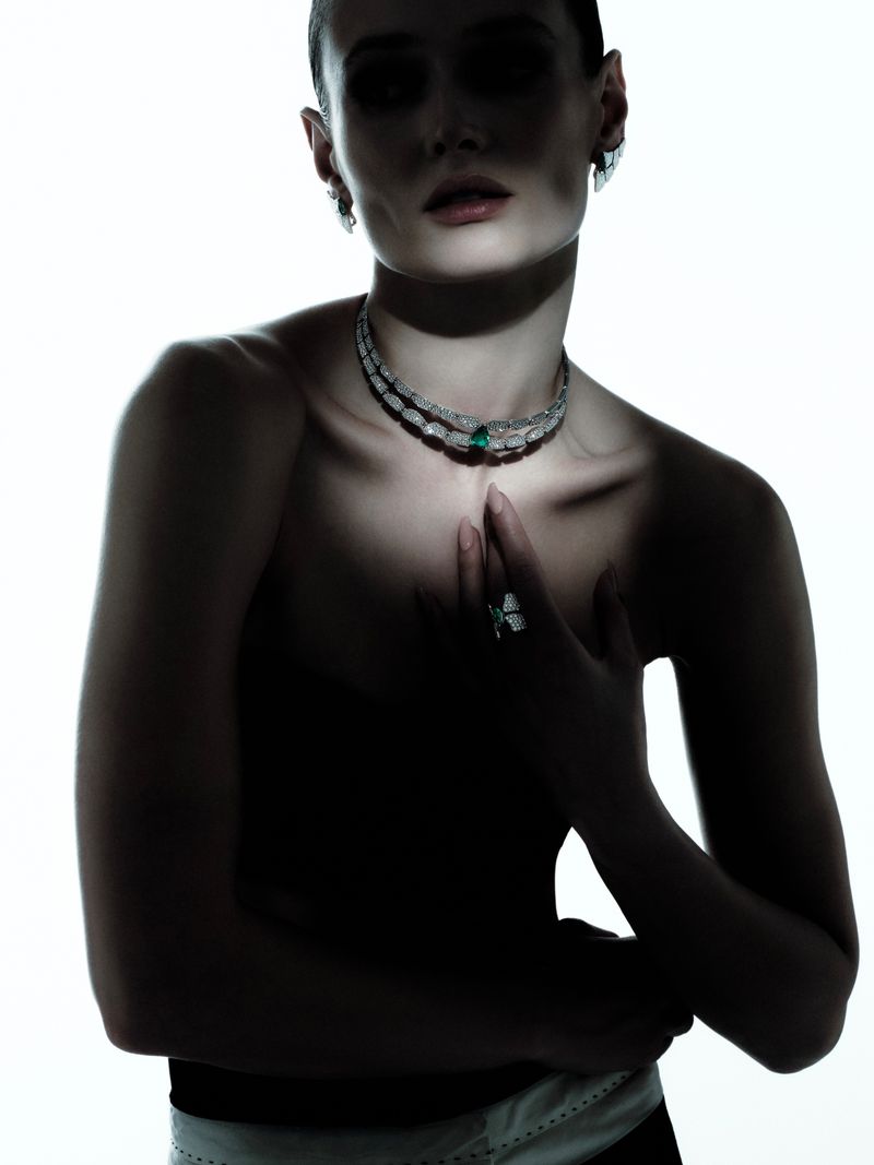 Close-up portrait of a model wearing diamond and emerald necklaces against a bright white background with dramatic lighting.