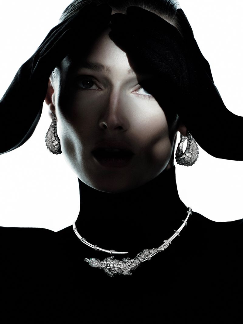 Headshot of a model wearing a black turtleneck and jewelry. Her hands are raised toward her face, and she is on a white backdrop.