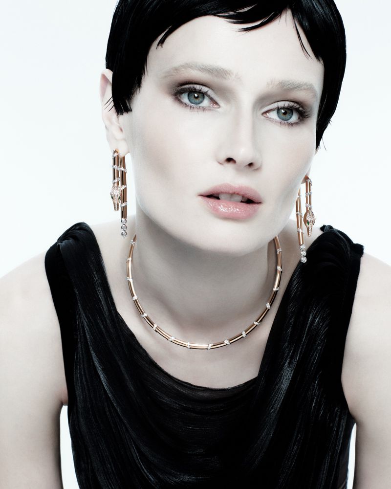Close-up portrait of a woman wearing gold jewellery and a black top against a plain white background for Orlov Jewelry S/S 26.